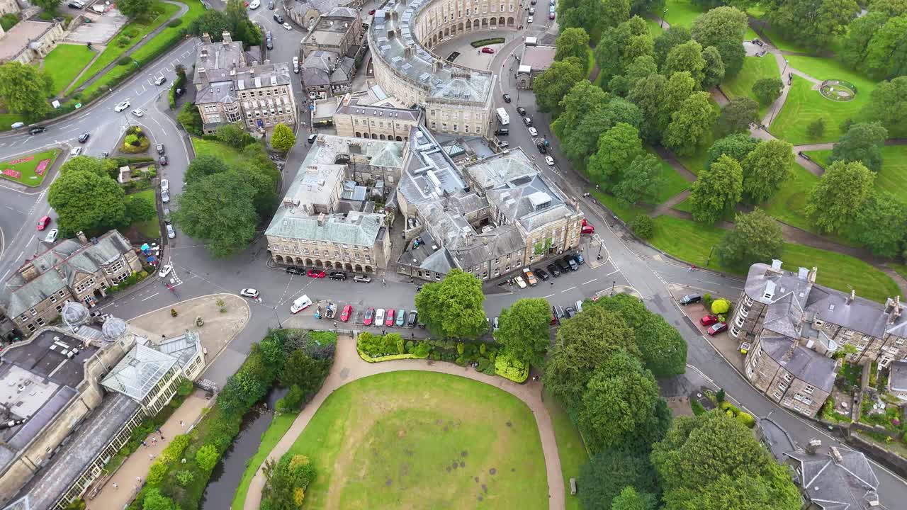 High-angle drone footage smoothly pans above Buxton’s iconic crescent, historic buildings, and lush parkland in soft daylight, revealing urban and natural details