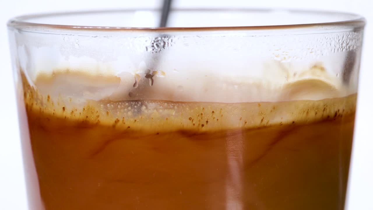 Grains of instant coffe falling into a glass of hot water and dissolving, macro shot close up view