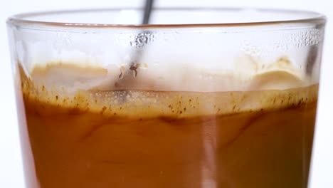 granos de café instantáneo que caen en un vaso de agua caliente y se disuelven, vista macro de primer plano