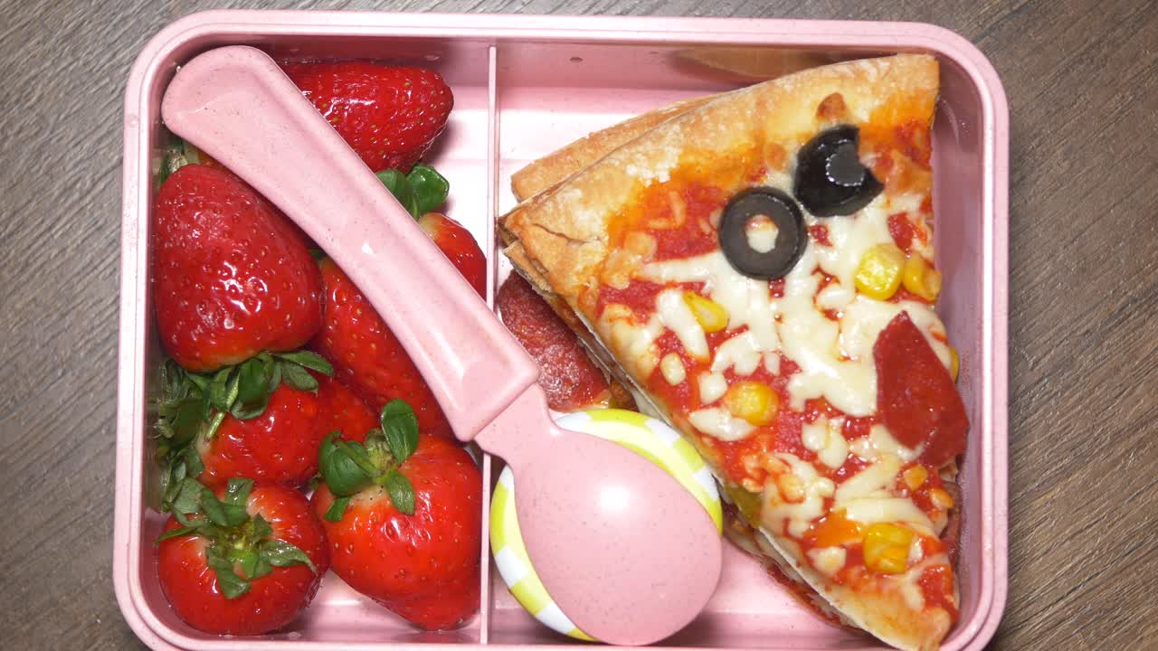 pizza y fresas en una caja de almuerzo rosa