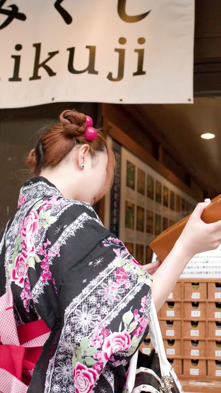 A woman in traditional kimono shakes a wooden box for fortune telling at a shrine