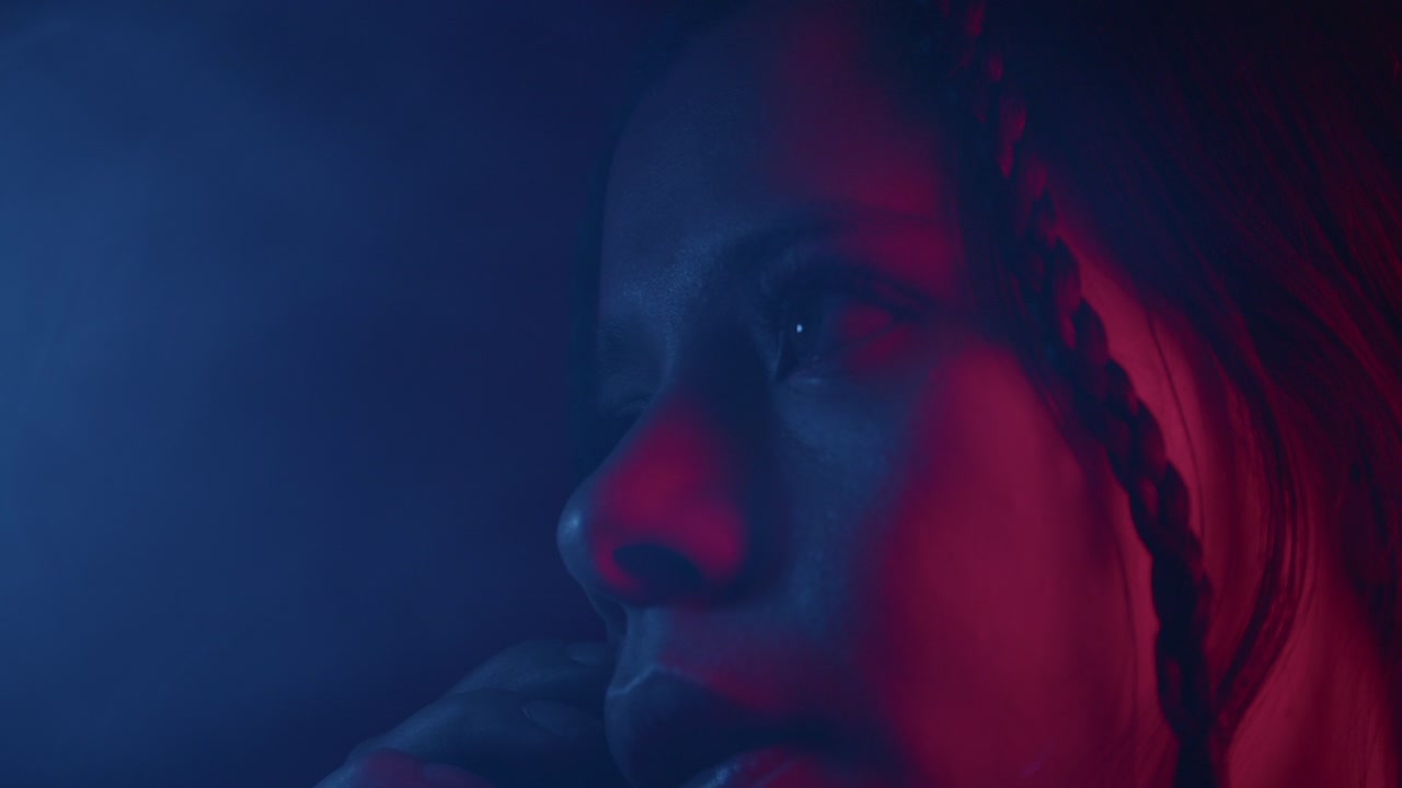 Moody close-up of a girl on a phone call, bathed in red and blue lighting, creating a dramatic and emotional atmosphere. Intimate and tense, the scene captures a moment of connection