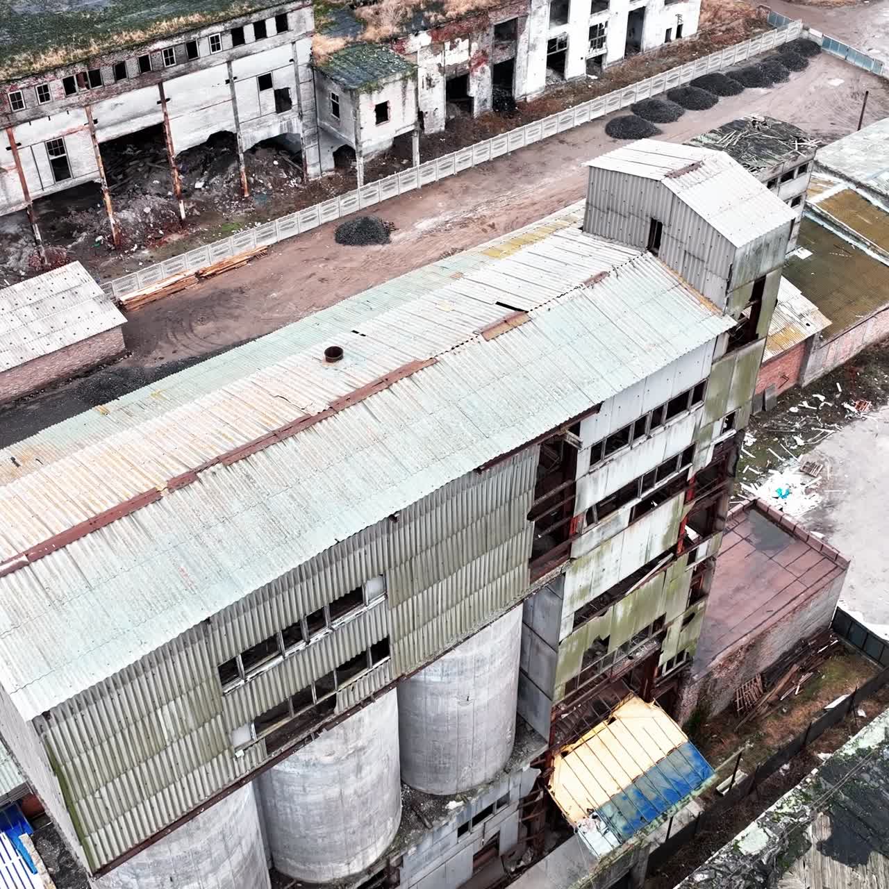 Ruined old factory buildings. Damaged walls, roofs and scattered debris. Aerial view. New modern building at the backdrop