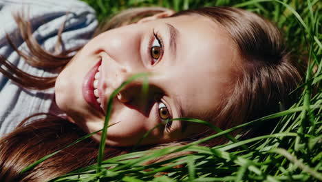 a young girl smiling while lying in green grass