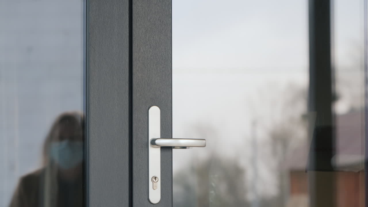 una mujer con una máscara protectora y guantes entrará por la puerta de la casa