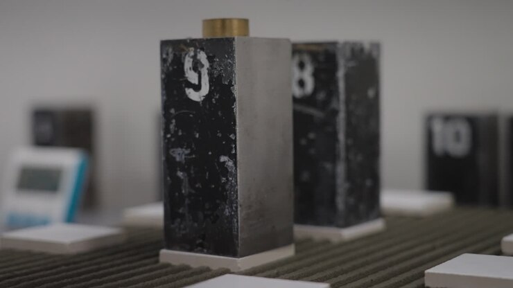 Hånd i latexhandske lægger vægte på en flise over cementblanding