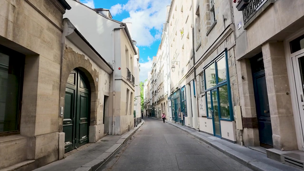 Et tracking-shot fra lav vinkel bevæger sig gennem en smal parisisk gyde under en lys himmel.