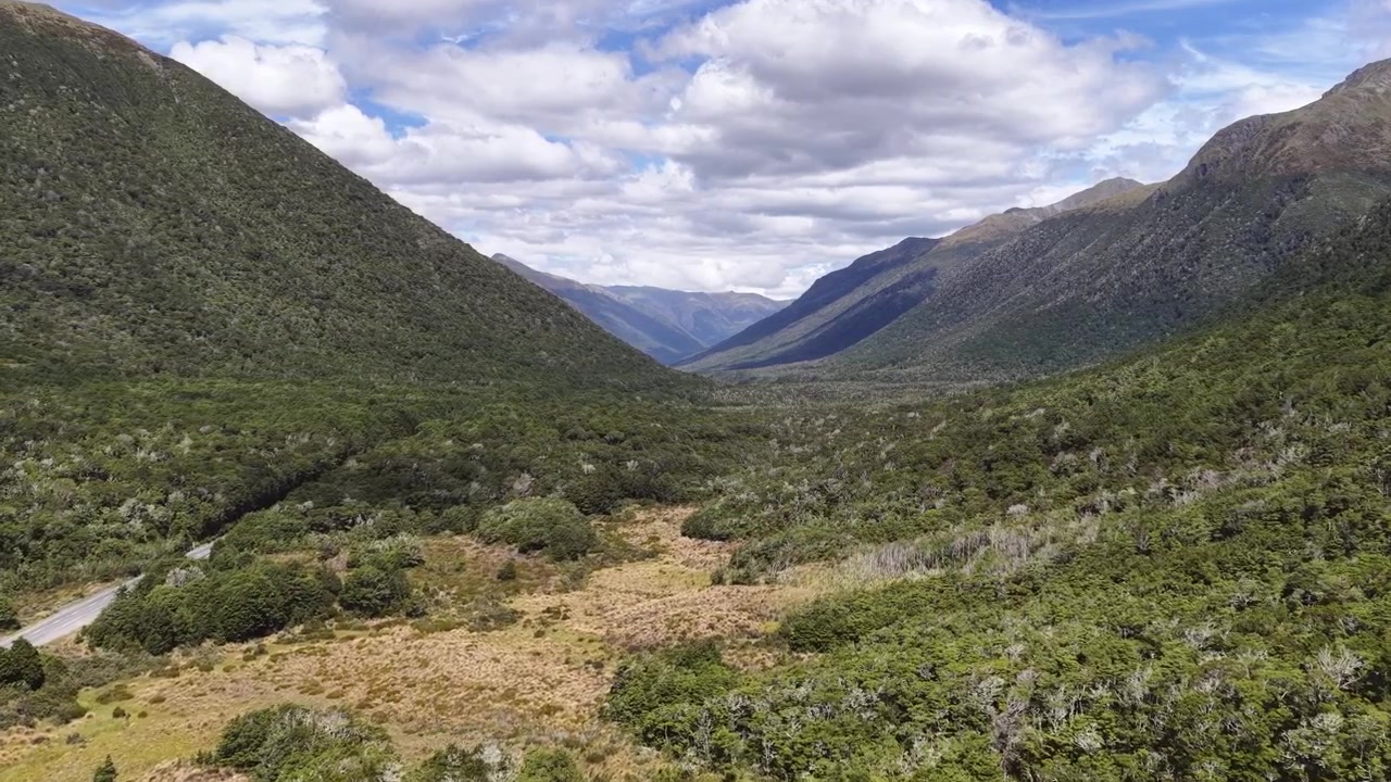 Riprese aeree con drone di una pittoresca valle di montagna con una strada sterrata tortuosa attraverso colline verdi e nuvole spettacolari nell'Isola del Sud della Nuova Zelanda.