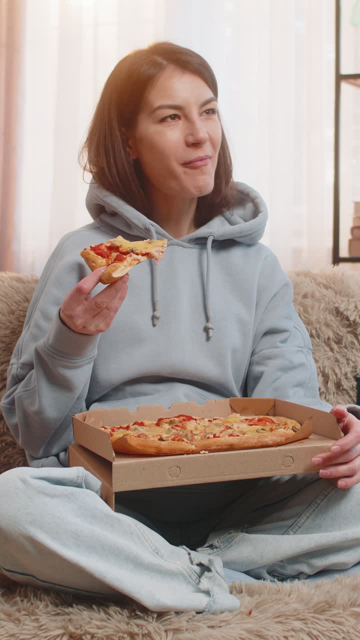 mujer joven comiendo deliciosa comida chatarra pizza y palomitas de maíz sentada en el sofá del sofá viendo la televisión en casa
