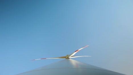 looking up from the base of a wind turbine, blades against clear blue sky