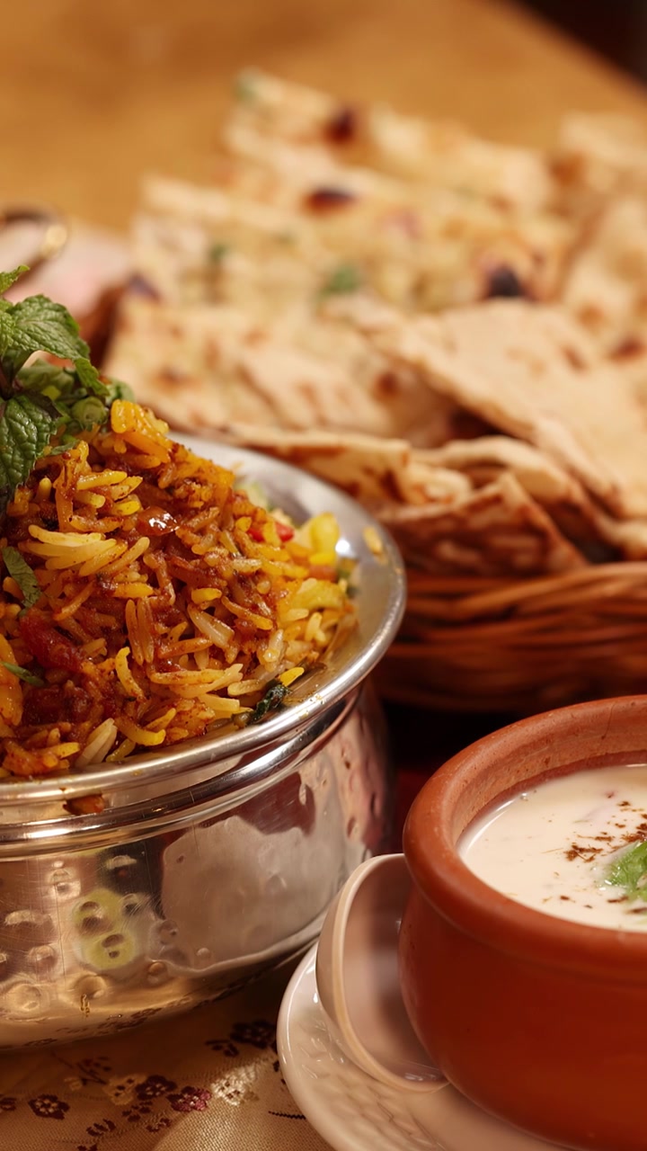 Nærbillede af kamerapanorering henover biryani-ris, naanbrød og raita-yoghurt i en restaurantindstilling.