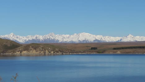 zoom estático de la hora dorada, a mediados de invierno, a través del hermoso lago alpino de color azul tinta hacia majestuosas montañas