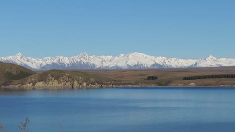 golden-hour, mid-winter, static zoom across beautiful inky-blue colored alpine lake towards majestic mountains