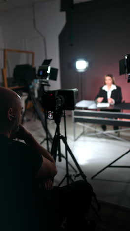 rear view of a cameraman sitting at camera. videographer taking video of a woman sitting at desk. vertical video.