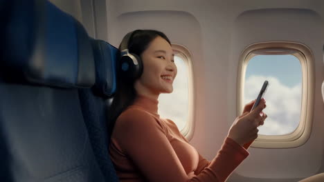 young woman enjoying in-flight entertainment with headphones and phone on an airplane