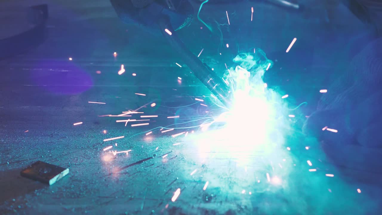 Close-up work with metal steel and iron using a welding machine, bright sparks and flashes in very slow motion