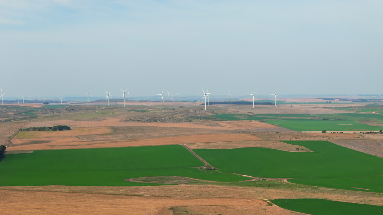 Aerial View Of Wind Farm Towers in the horizon and Countryside Fields, brown and green agriculture, copy space and slow motion