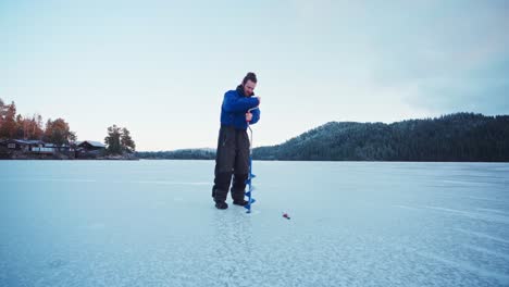 man drilling on ice using auger drill - ice fishing at frozen lake in winter at norway