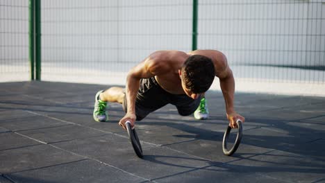 Un-Hombre-Fuerte-Y-Musculoso-Está-Haciendo-Flexiones-Con-Anillos