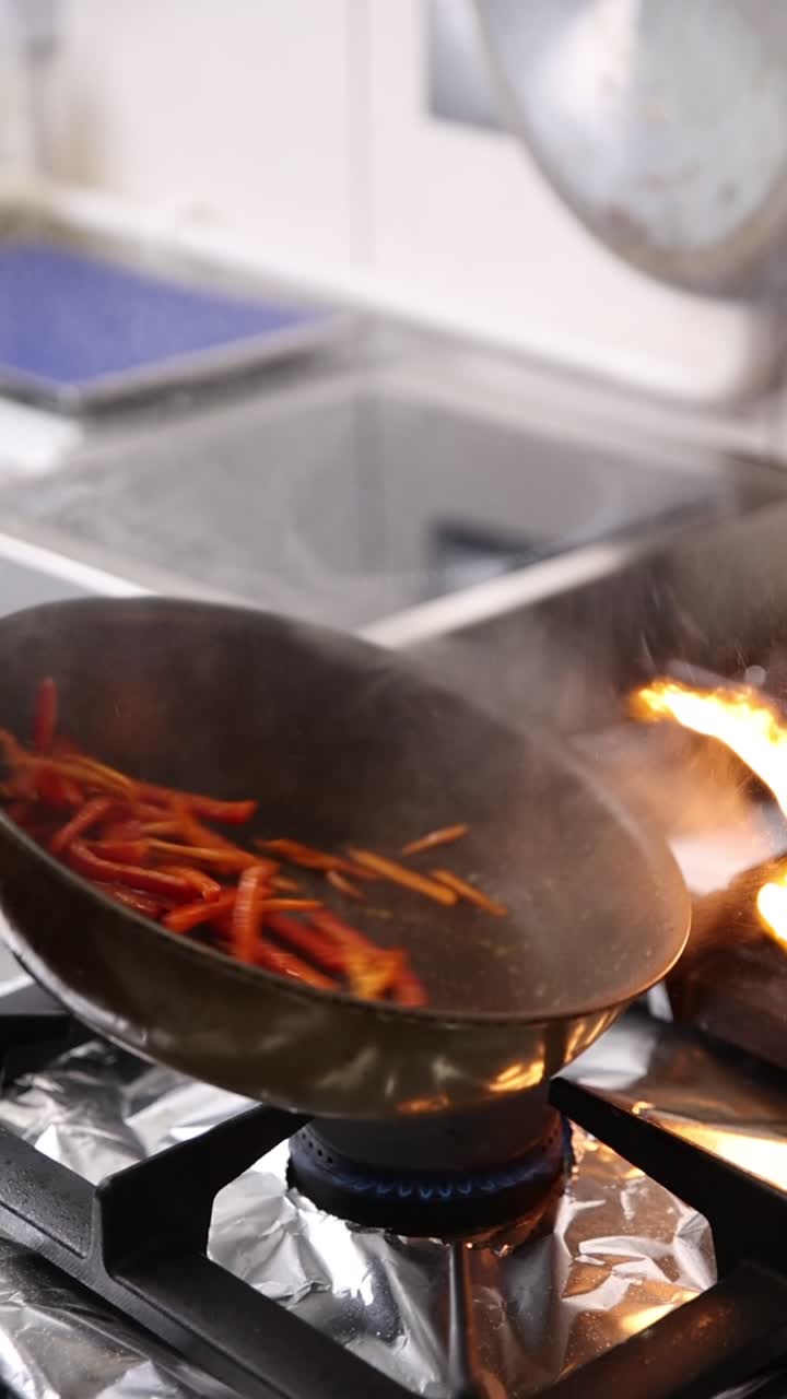 Saltare in padella peperoni rossi e verdure in una padella fiammeggiante.