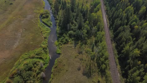 tilt down aerial shot over river and railroad with alpine forest near 127 mile house, canada