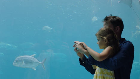 padre con su hija en el acuario tomando fotos de peces usando un teléfono inteligente disfrutando de la vida marina nadando en el tanque divirtiéndose en el oceanario compartiendo en las redes sociales