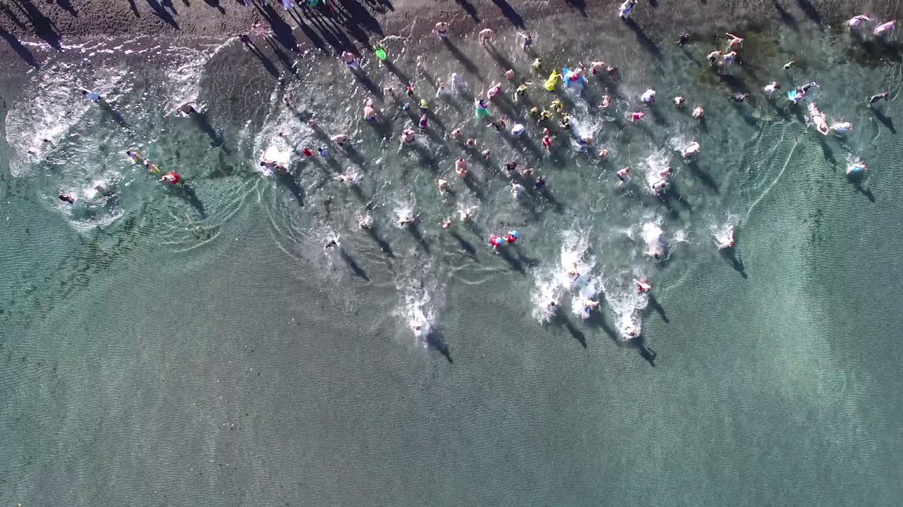 People running into clear water of Lake Taupo in New Zealand on summer day, crowd splashing