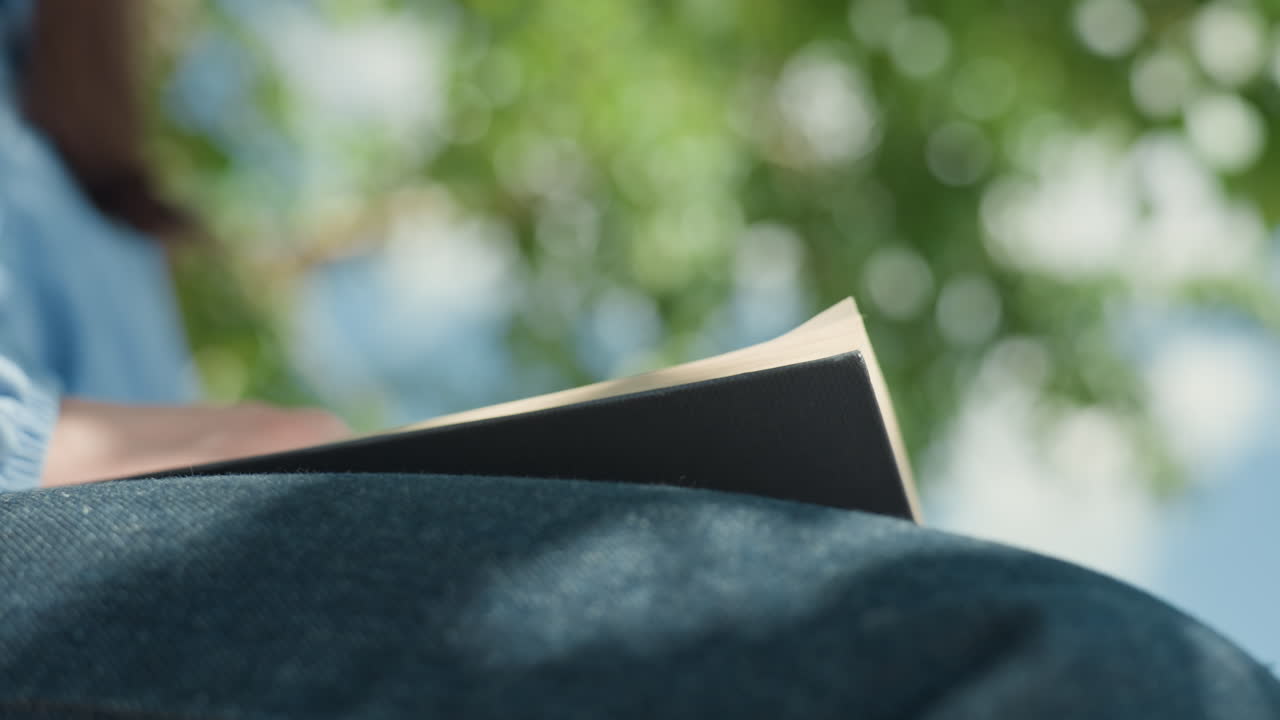 고요한 야외 세션을 즐기는 차분한 사람, 햇빛이 드는 잎이 무성한 덮개 아래에서 독서에 몰두하는 평온한 사람, 나무의 넉넉한 그늘 아래에서 무릎에 책을 올려놓고 페이지를 부드럽게 넘기는 편안한 독서가