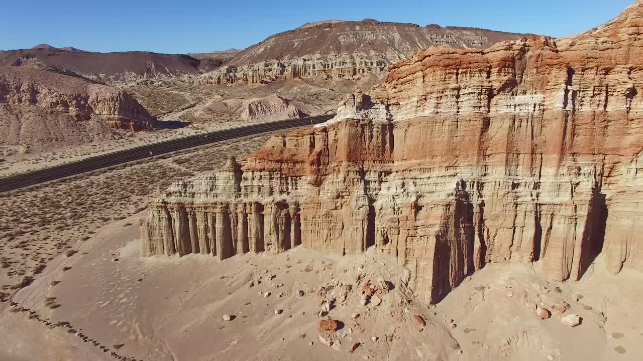 una antena sobre un paisaje desértico con un camión de 18 ruedas moviéndose a lo largo de una carretera en la distancia