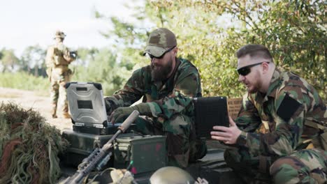 los soldados que pertenecen a un ejército poderoso están preparando una estrategia para luchar contra el enemigo sorpresa ingresar datos en el sistema hablar sostener la tableta vestidos con uniformes moro, camuflaje, cascos, mochilas, campo de entrenamiento