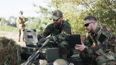 soldiers belonging to powerful army are preparing strategy to fight surprise enemy enter data into system talk hold tablet dressed in uniforms moro, camouflage, helmets, backpacks, training ground