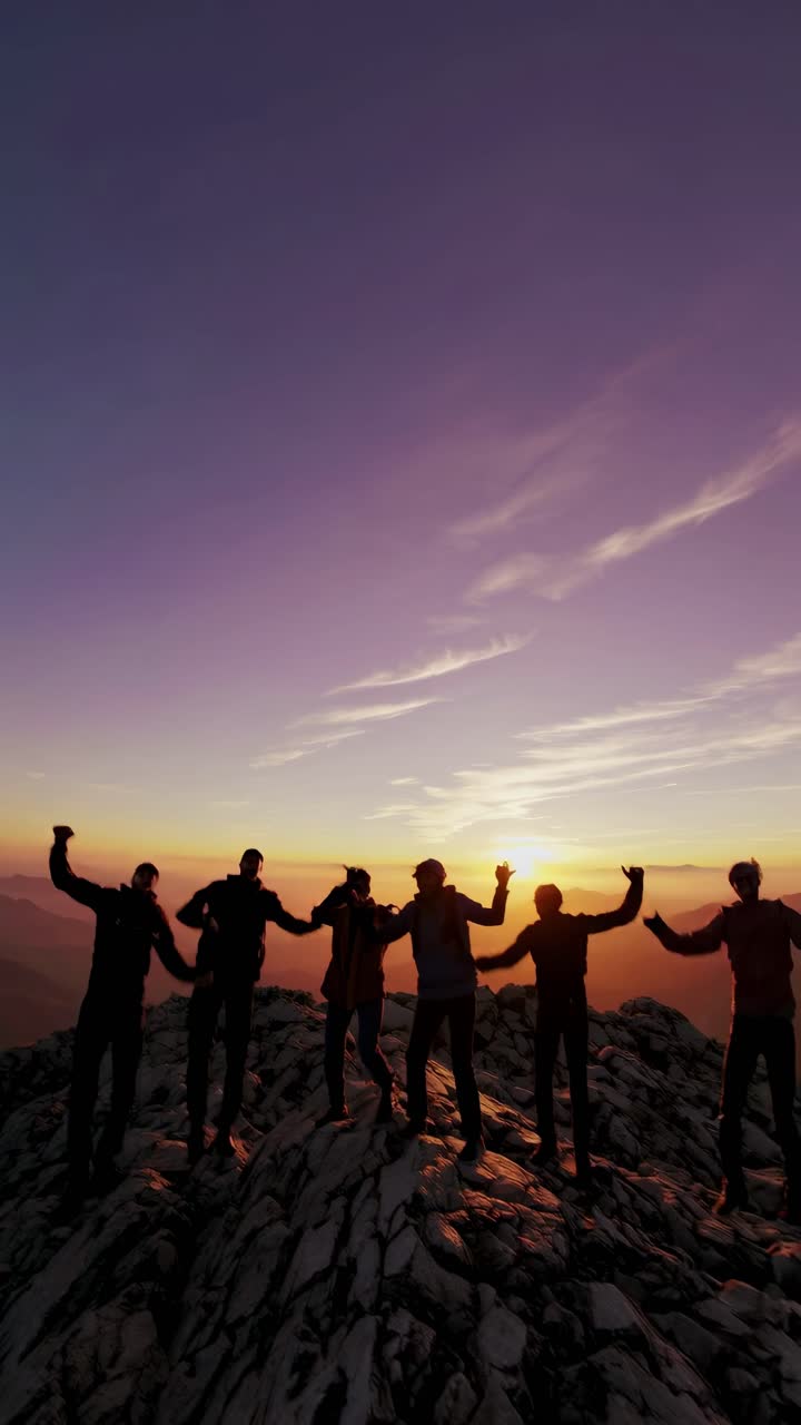Silhouetted group celebrating atop a mountain at sunset, captured from a low angle