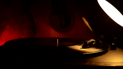 slider shot. disco de vinilo vintage tocando en el reproductor y la guitarra acústica en el fondo con humo de naranja de fuego. concepto de crimen o blues con instalación de automóvil de juguete. enfoque selectivo