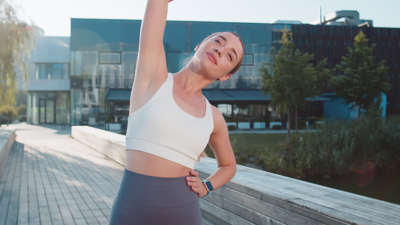 Caucasian sporty young woman runner stretching arms warm up before jogging in city park on sunny day