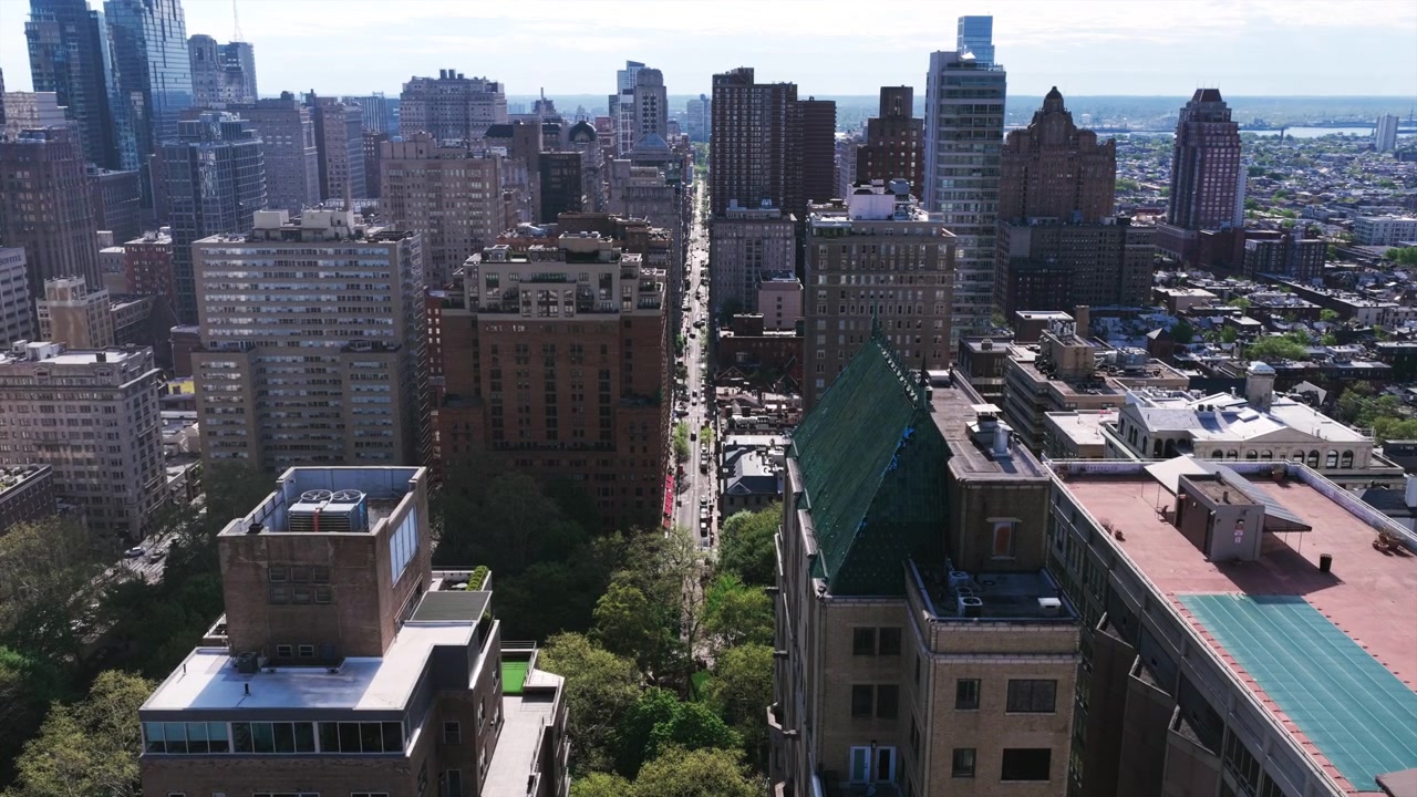 Veduta aerea con drone che guarda lungo un viale di Filadelfia fiancheggiato da grattacieli, alberi lussureggianti di un parco verde e lo skyline del centro che si estende fino all'orizzonte.