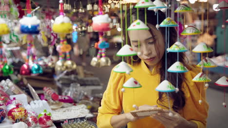 Vietnamese-female-tourist-in-yellow-dress-buying-souvenirs-at-market-stall-in-Hoi-An,-Vietnam