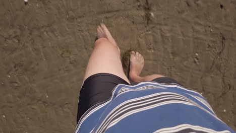 first-person view of a man walking on wet sand, blue polo shirt and black shorts