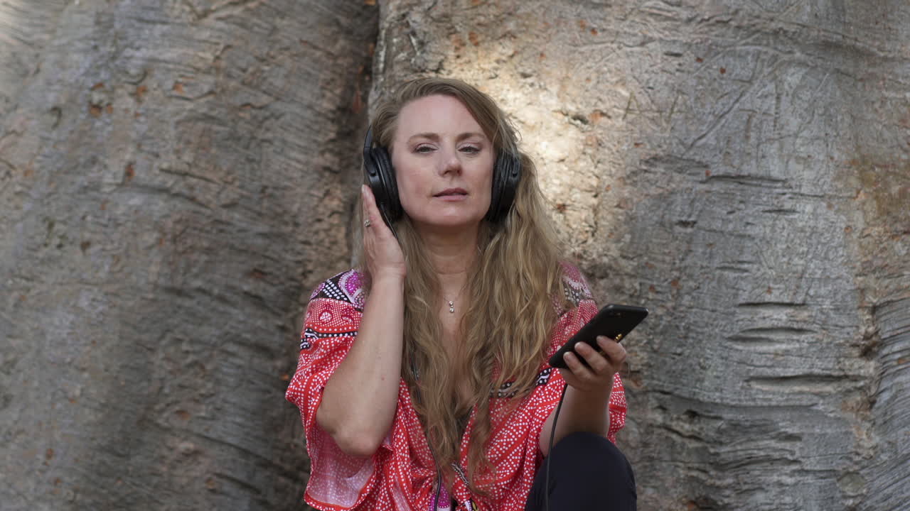 Attractive, smiling woman enjoying music in headphones while sitting in the park
