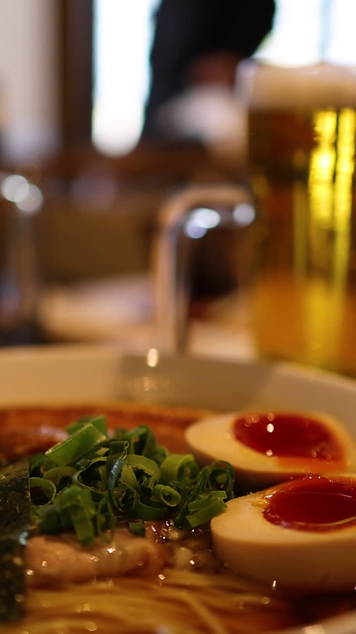 Primo piano di una ciotola di ramen con birra sullo sfondo