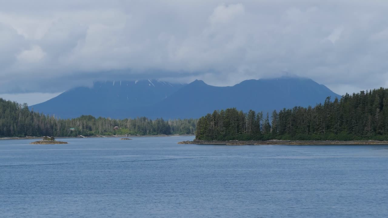 Landscape around Sitka, Alaska, Alexander archipelago, with mountains covered by clouds and rocky islands covered by pine tree forest.