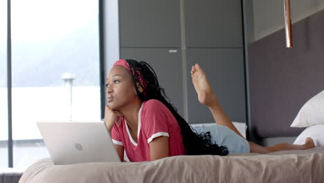 A-young-African-American-woman-lying-on-bed,-looking-at-laptop