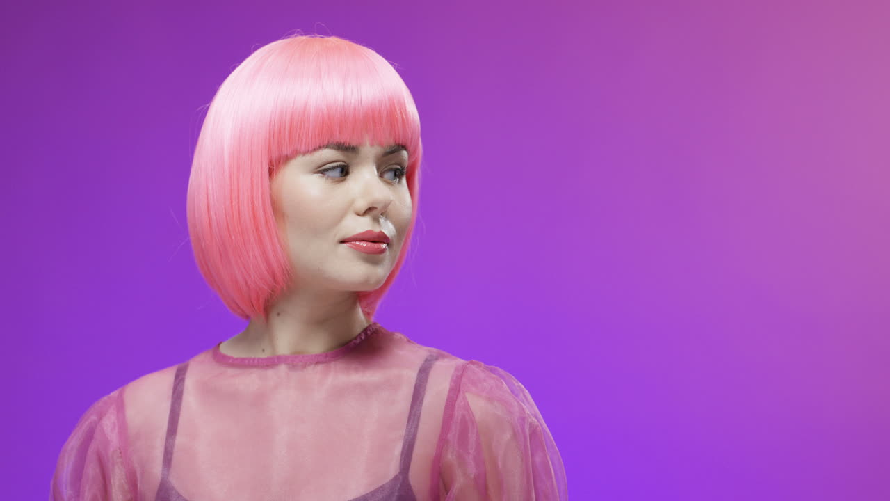 분홍색 가발을 쓰고 포즈를 취하고 벨벳 배경에서 카메라에 미소를 짓고 있는 매력적인 여성의 초상화