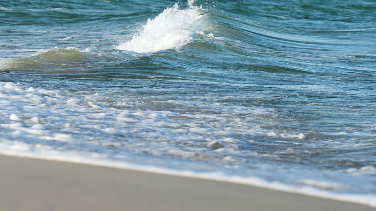 바다의 힘과 평온을 보여주는 모래 해변에 부히는 거품 같은 파도의 클로즈업