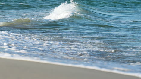 Close-up-of-a-frothy-wave-crashing-onto-the-sandy-shore,-showcasing-the-power-and-tranquility-of-the-sea