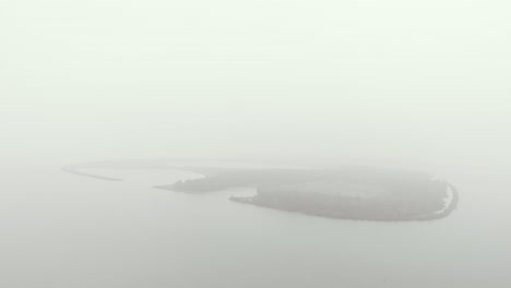 aerial view of a mysterious and in mist banks covered oval shaped island backing slowly away from it