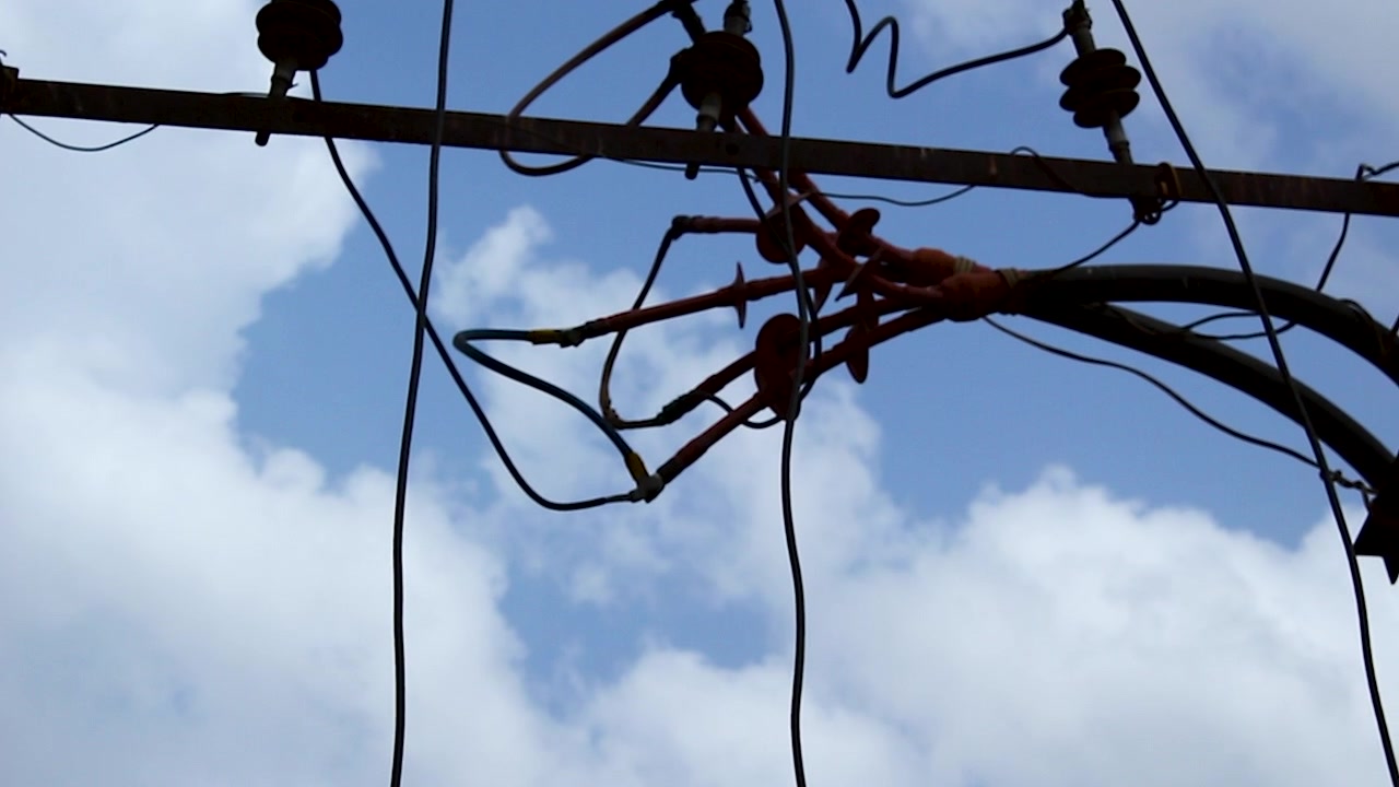 Tilt up footage of electrical distribution lines and utility transformer infrastructure against a cloudy sky, ideal for energy, power grid, electricity supply, and infrastructure projects.