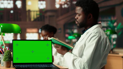 medical student uses books in the campus study space next to green screen