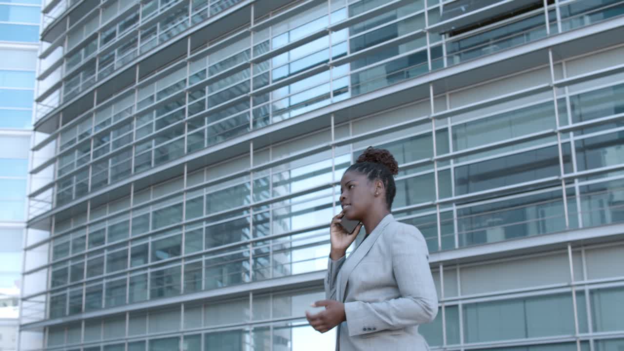 Side view of a confident African American businesswoman walking and talking on mobile phone outside office buildings
