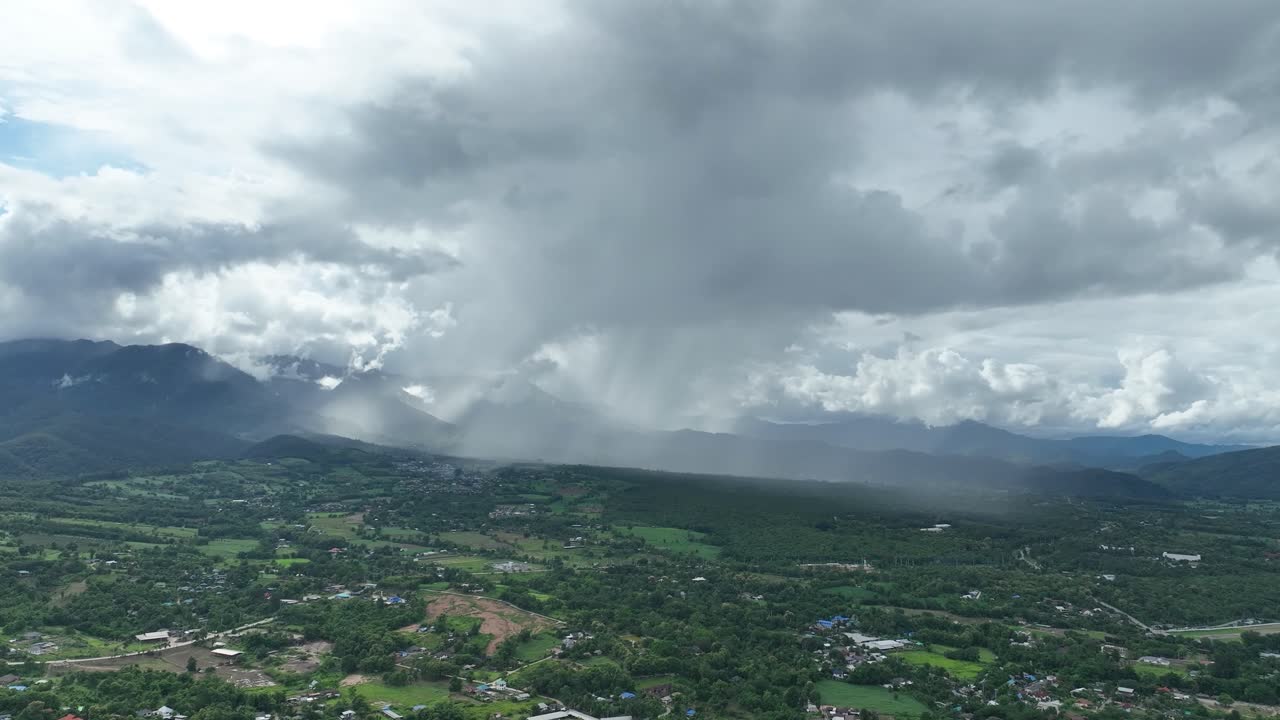 Aerial footage, Pai in northern Thailand shows sweeping valley landscape with storm clouds releasing. A dramatic contrast of light and shadow captures nature’s intensity in a peaceful rural setting