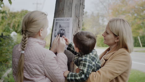 a woman with two children attaches a leaflet about a missing cat to a pole